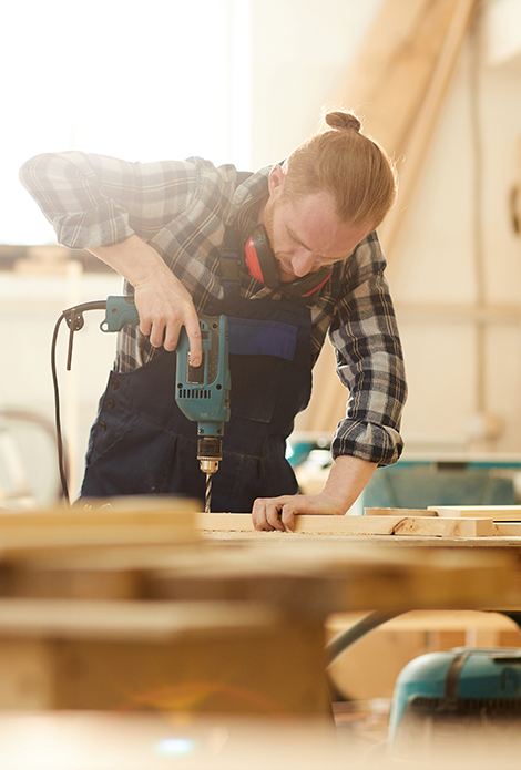 Man drilling a wooden board with PPE equipment on